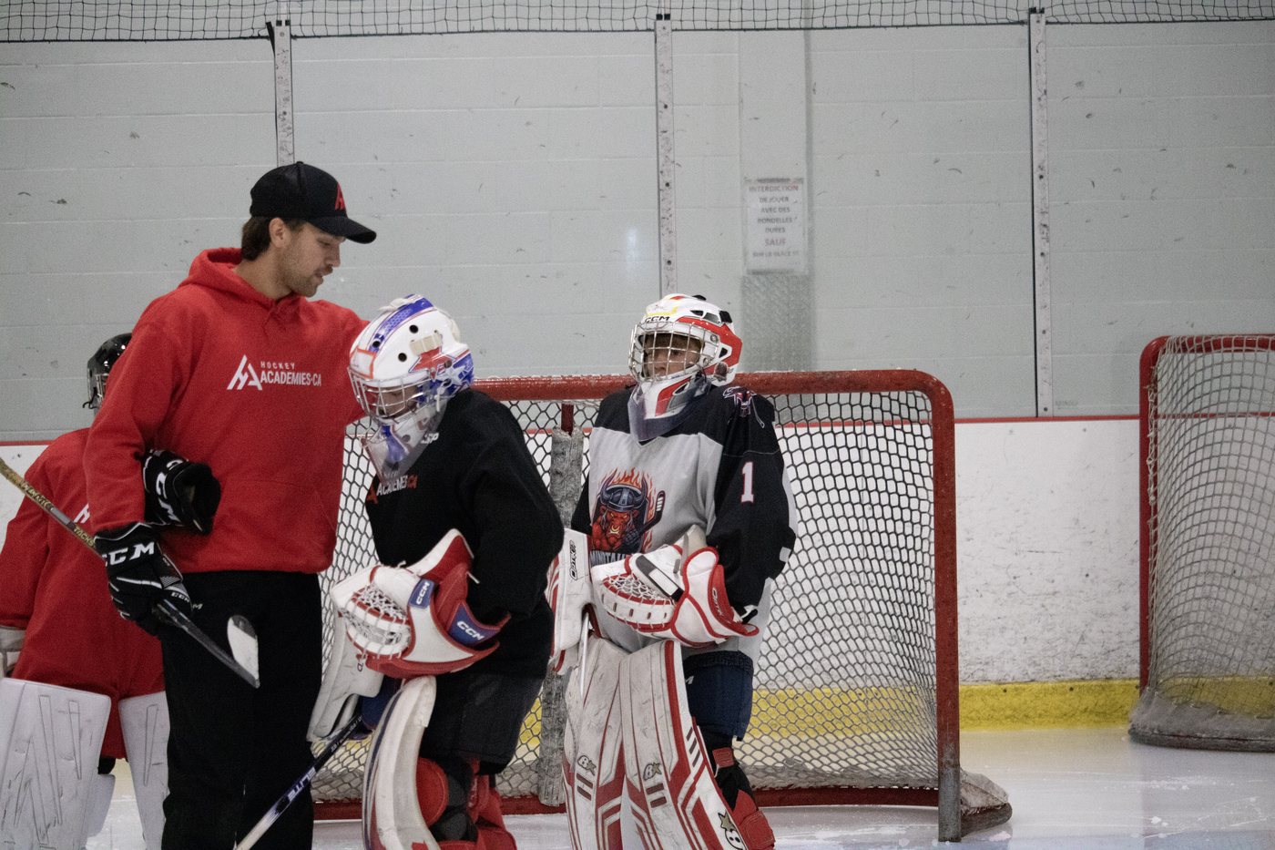 Un entraîneur de Hockey-Académie discute avec deux jeunes gardiens devant le filet